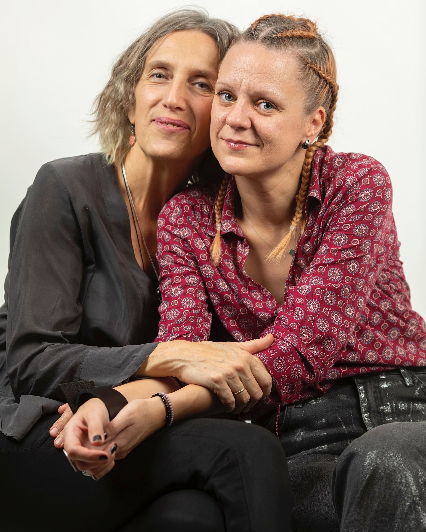 Portrait of two women embracing and smiling at the camera against a plain light grey background