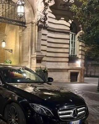 A black car parked in front of a building lit for the evening