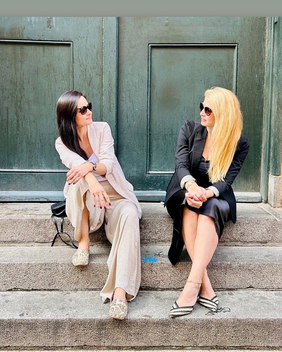 Marija and Maja sitting together on the stone steps of an old building with a green door