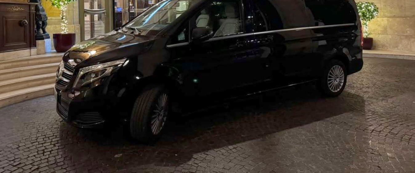 A black minivan waiting at a hotel entrance in the evening
